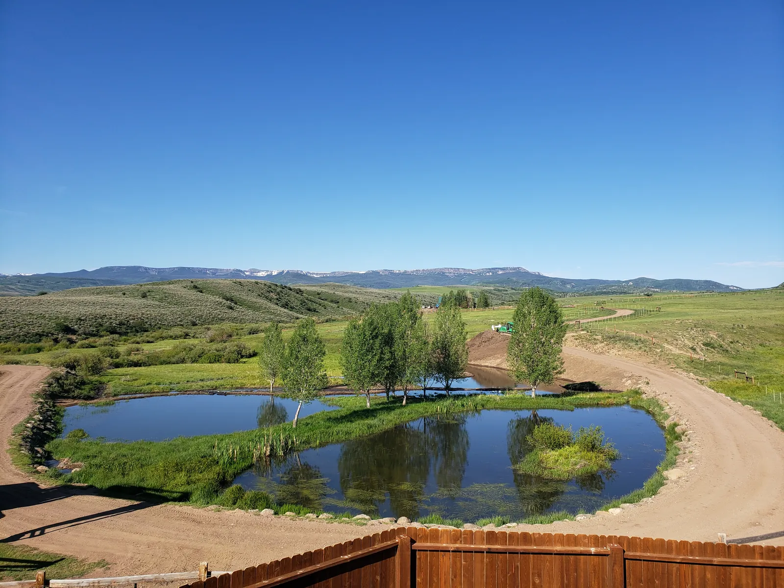 A two-lobed pond with an island and young aspens, flat-topped mountains on the horizon