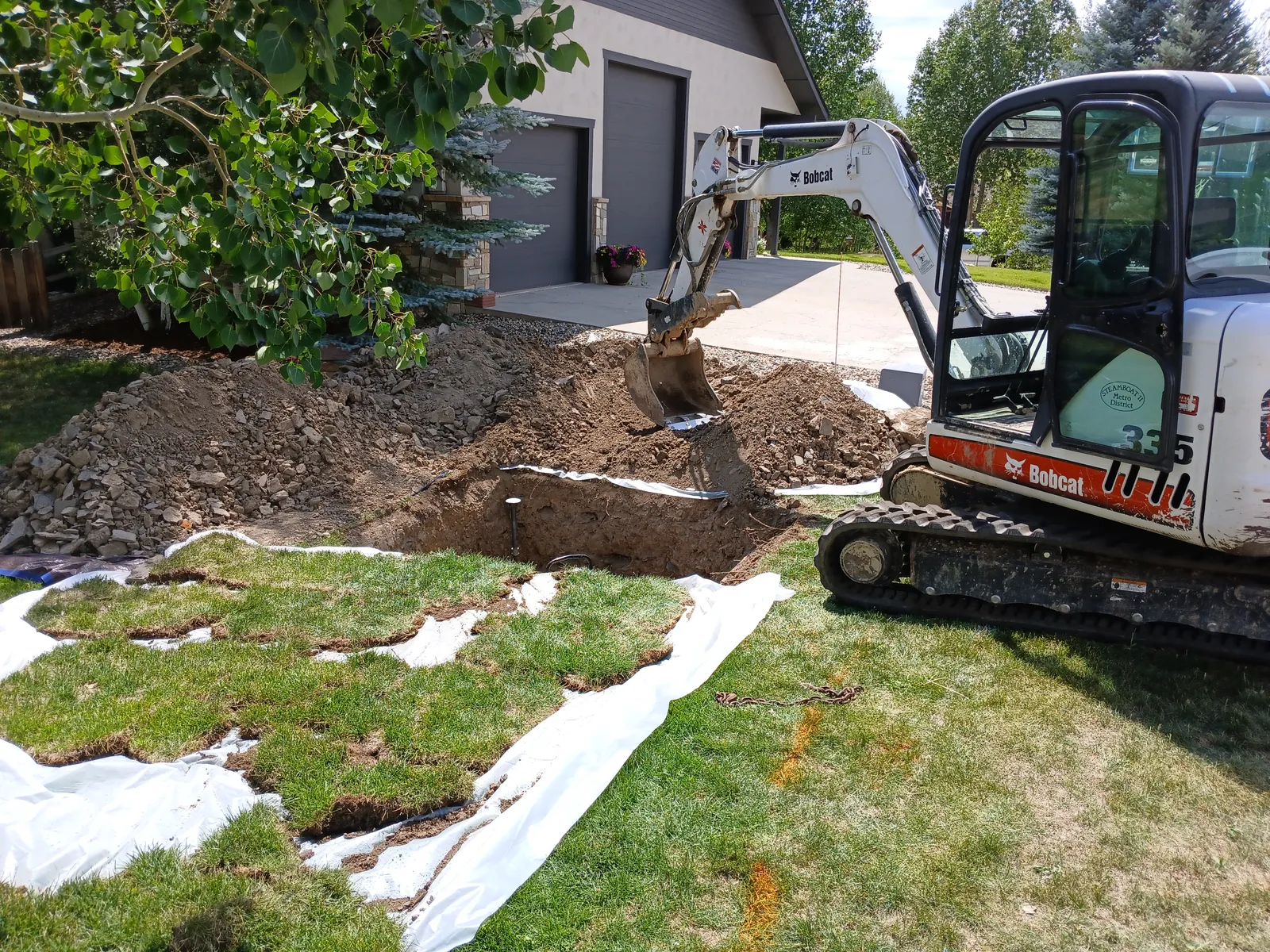 Mini excavator digging in a lawn, cut sod rolled back onto tarps
